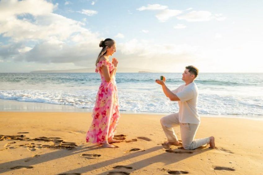 Una playa con una persona arrodillada proponiendo matrimonio a otra persona de pie con las manos entrelazadas. 5