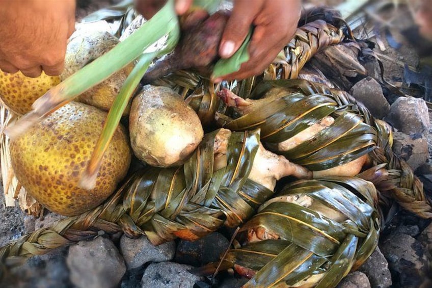 A person preparing food wrapped in leaves over a fire. 3
