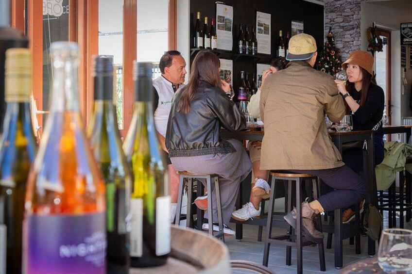 Eine Bar mit Tischen, an denen Personen sitzen, Weinflaschen und ein Weihnachtsbaum im Hintergrund. 4