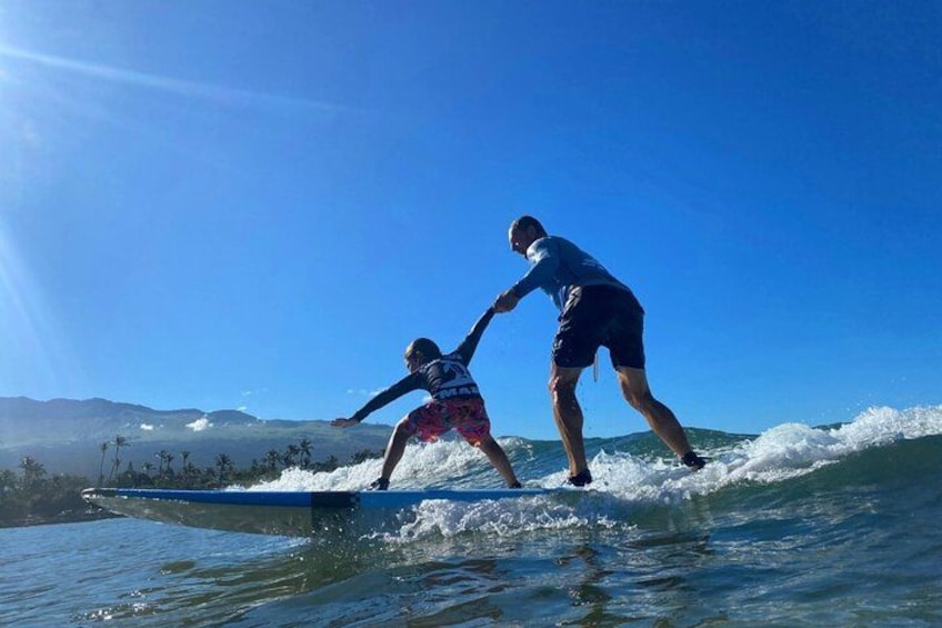 Two people surfing on a wave with a clear blue sky and mountains in the background. 2