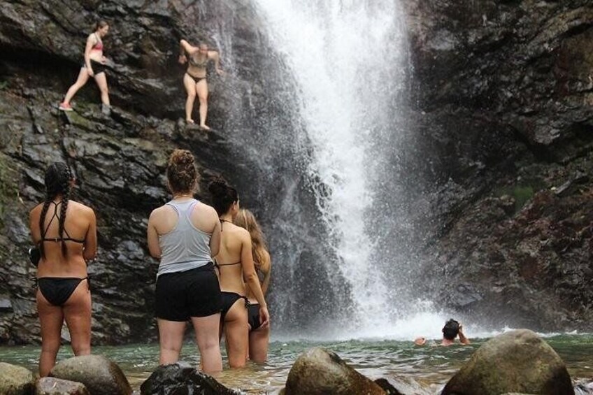A group of people standing by a waterfall, some preparing to jump into the water. 3