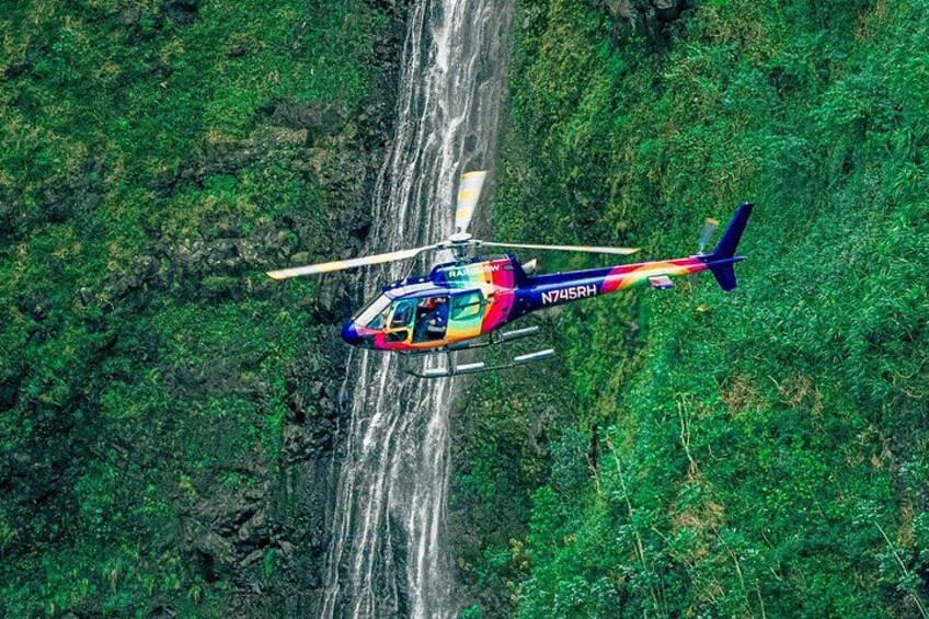 A colorful helicopter flying over a lush green landscape with a waterfall. 1