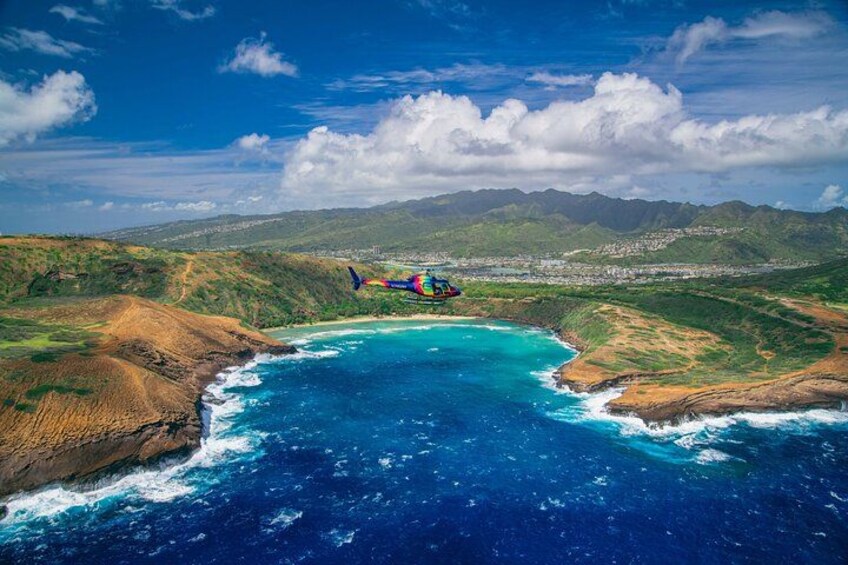 A helicopter flying over a coastal area with a clear view of the ocean and distant mountains. 2