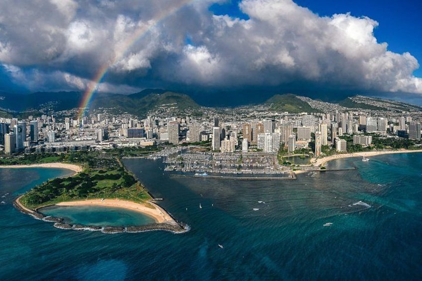 A coastal cityscape with a prominent rainbow, dense urban buildings, and a bay with a small island. 5