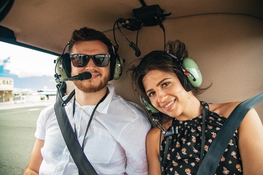Two people wearing headsets inside a vehicle, with a building and a clear sky in the background. 3