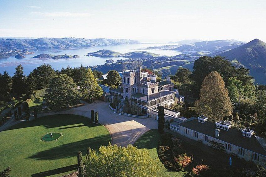 Una extensa propiedad con una imponente estructura tipo castillo, amplios jardines verdes y una vista panorámica de un lago y montañas. 4