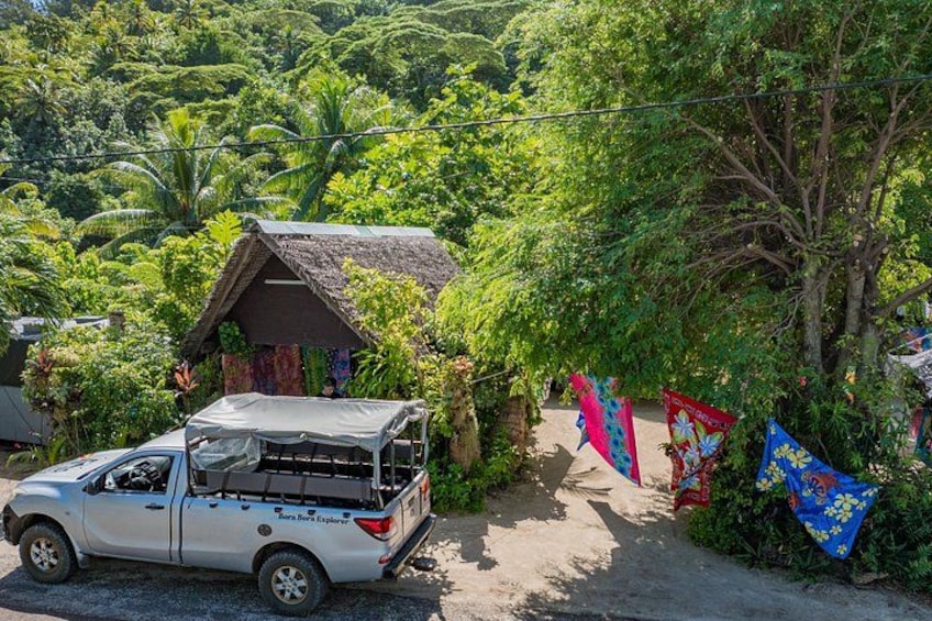 A white pickup truck parked near a thatched-roof hut surrounded by lush greenery and colorful flags. 2