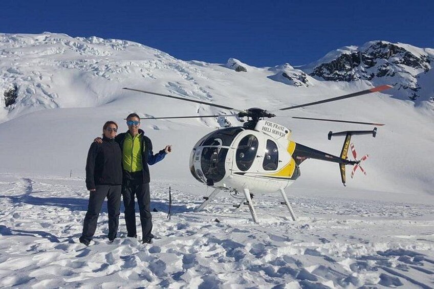 Two people standing in front of a helicopter on a snowy mountain. 2