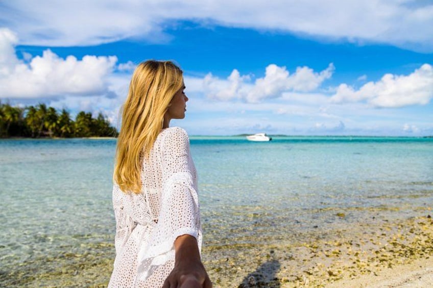 En person står på en strand med klart vand og en båd i det fjerne. 1
