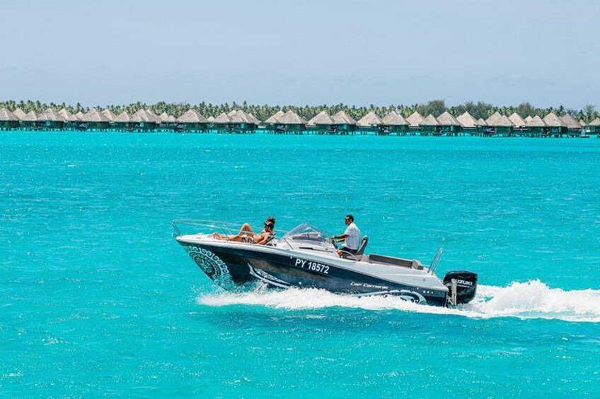 Un bote a motor rápido con dos personas a bordo, navegando por aguas turquesas con bungalows sobre el agua al fondo. 3