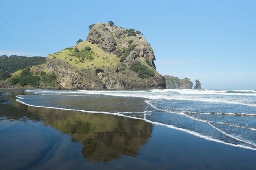 A beach with a large rock formation, waves crashing onto the shore, and a clear sky. 1
