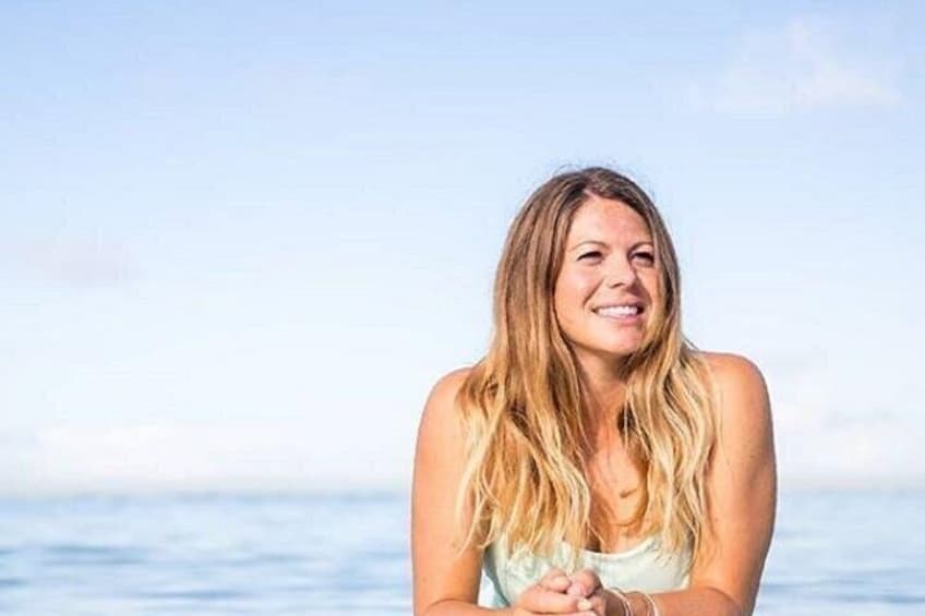 A person with long hair, wearing a light-colored top, standing by a body of water. 2
