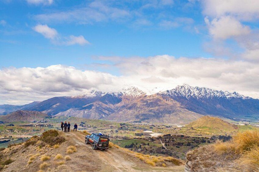 A mountainous landscape with a clear sky, a dirt road, and a vehicle with people in the distance. 1