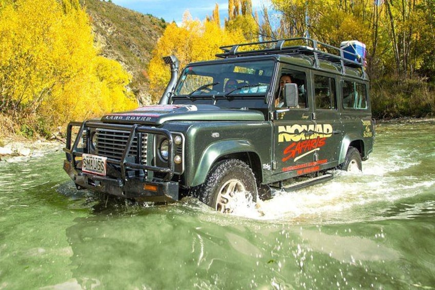 A Land Rover driving through a river surrounded by autumn-colored trees. 5