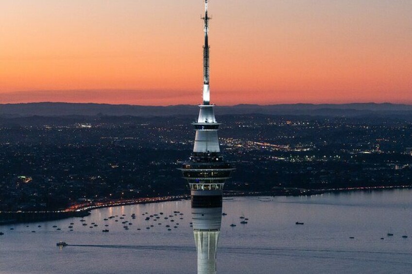 Een toren met een verlichte weerspiegeling in het water, omgeven door een stadsgezicht in de schemering. 2