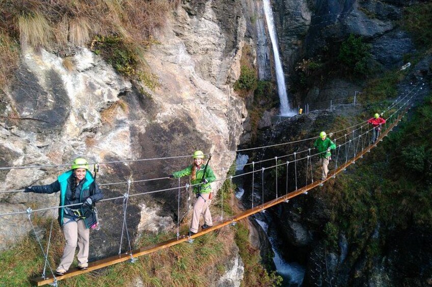 A group of people crossing a suspension bridge over a canyon with a waterfall. 4