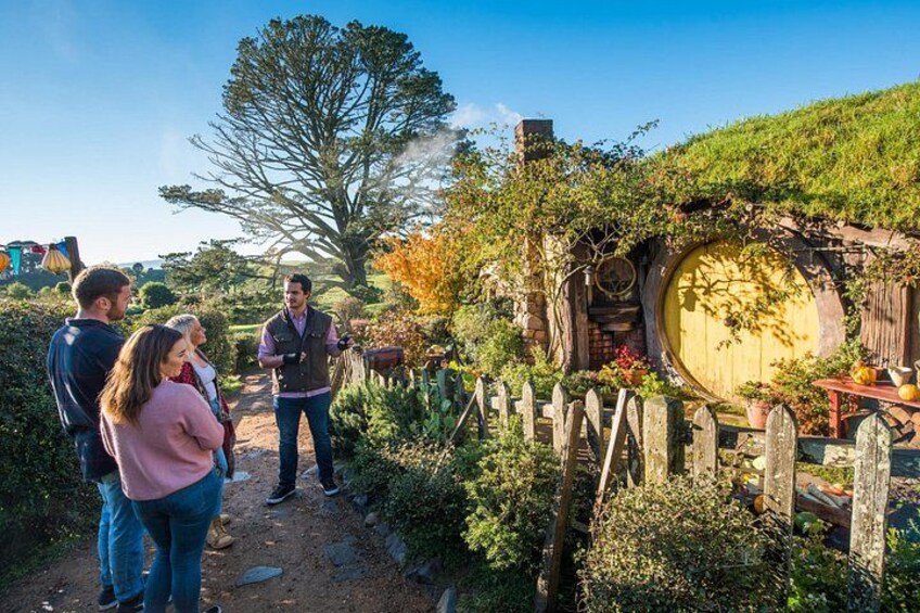 Un jardín de temática Hobbiton con una puerta redonda, valla de madera y abundante vegetación. 4