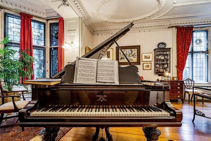 A grand piano in a room with red curtains, a chandelier, and framed pictures on the wall. 4