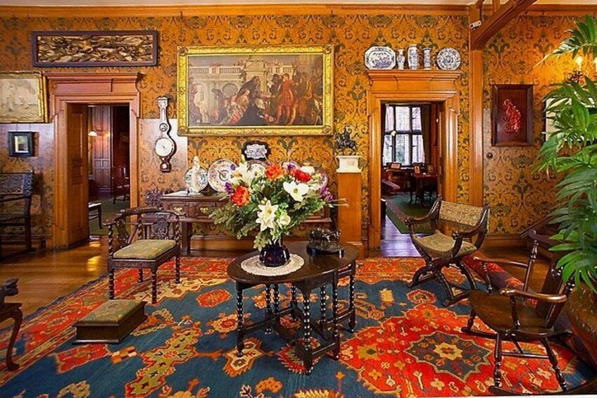 A richly decorated room with ornate wallpaper, a large painting, and a floral arrangement on a table. 2
