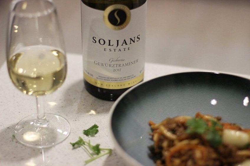 Una copa de vino, una botella de Soljans Estate Gewürztraminer 2017 y un bol de comida sobre una mesa. 1