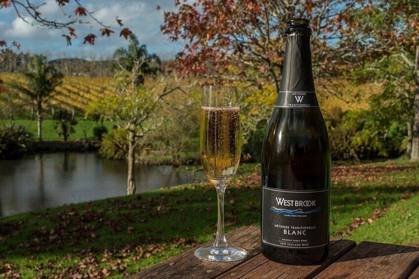 Una botella de Merlot Blanc de Westbrook y una copa de vino sobre una mesa de madera, con vistas panorámicas a un lago y follaje otoñal. 5