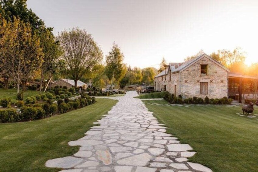 A stone pathway leading to a stone building, surrounded by well-manicured lawns and trees. 3