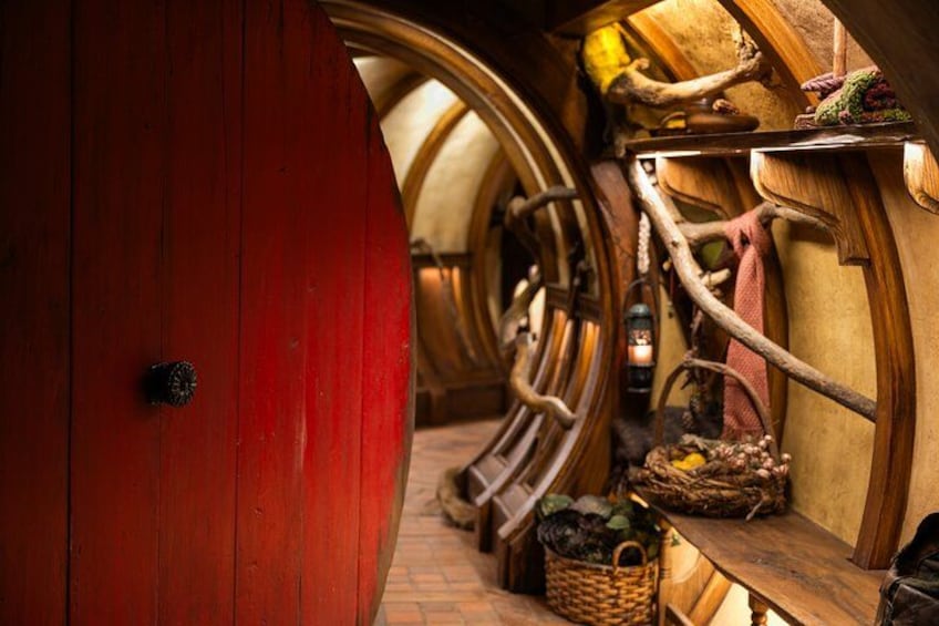 A wooden barrel-shaped room with a red door, a ladder, and shelves with various items. 2