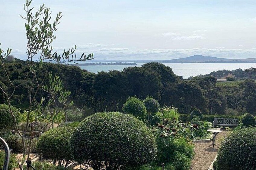 A landscaped garden with neatly trimmed bushes, a small bridge, and a view of a body of water and distant mountains. 2