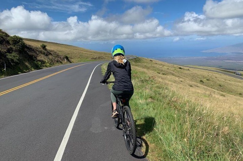 A person riding a bicycle on a road with grassy hills on the side. 5