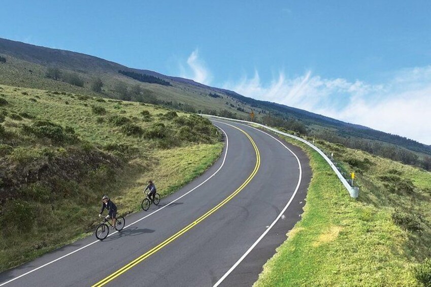 Una carretera sinuosa con ciclistas, colinas cubiertas de hierba y un cielo despejado. 2