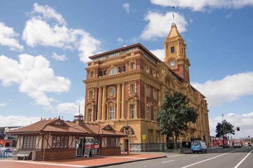 A large, ornate building with a clock tower, a red-roofed structure in front, and a clear blue sky with clouds. 4