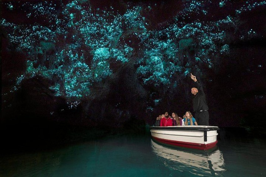 Ein Boot mit Personen auf dem Wasser, umgeben von einer Höhle mit blau leuchtenden Algen. 2