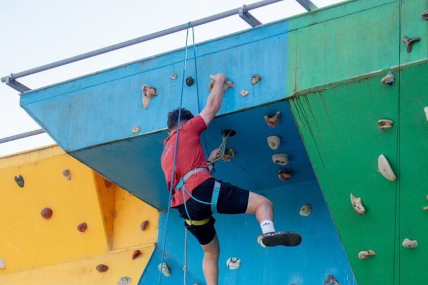 A person climbing a multi-colored rock climbing wall with various holds. 3