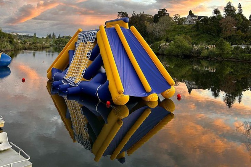 Un tobogán inflable azul y amarillo sobre agua, rodeado de follaje y una casa al fondo. 5