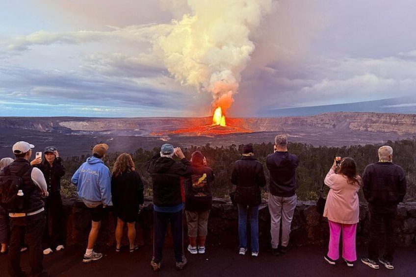 Un gruppo di persone osserva un'eruzione vulcanica con lava che scorre da un cratere. 3