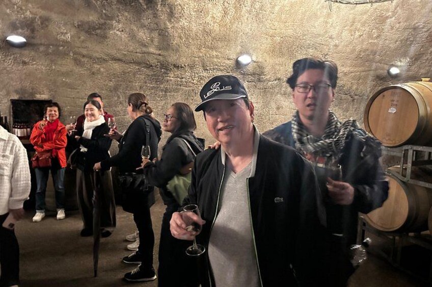 A group of people in a wine cellar with barrels and bottles. 3