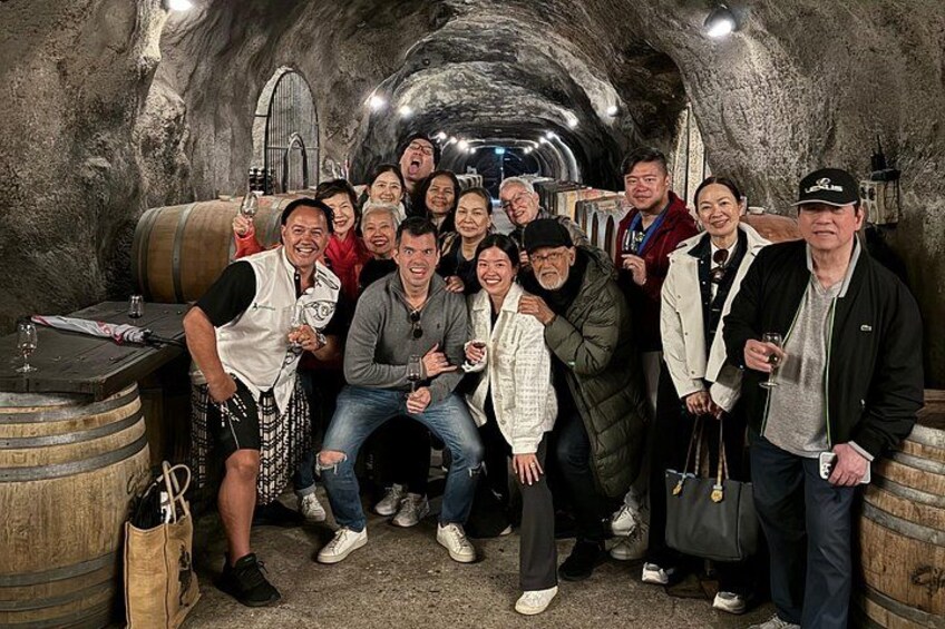 A group of people in a wine cellar with wooden barrels and a rustic interior. 2
