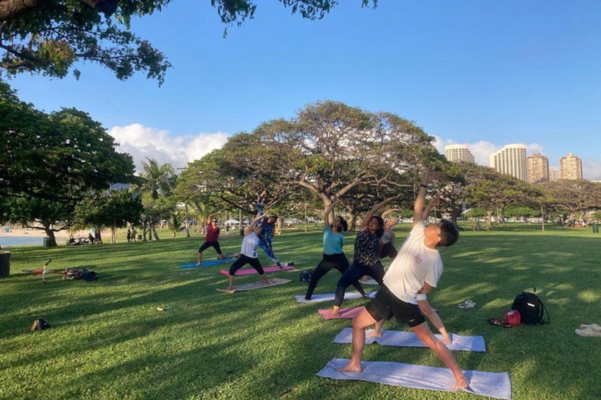 Des personnes pratiquent le yoga dans un parc, avec des arbres et des bâtiments en arrière-plan. 5