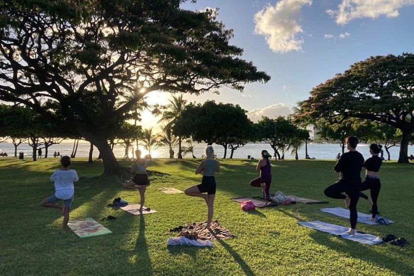 Un gruppo di persone che pratica yoga su tappetini in un parco, sullo sfondo alberi e uno specchio d'acqua. 3