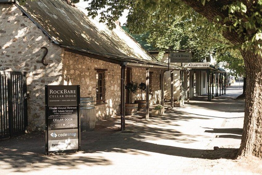 A stone building with a sign for RockBare Cellar Door, a Charity Shop, and a Thiele House Retreat. 1
