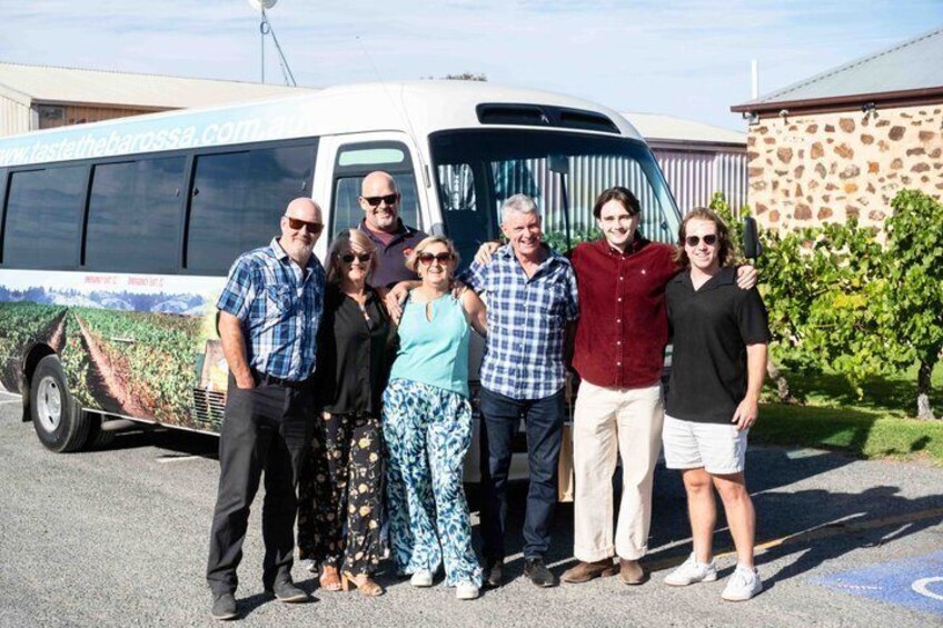 A group of people standing in front of a bus with a vineyard advertisement. 1