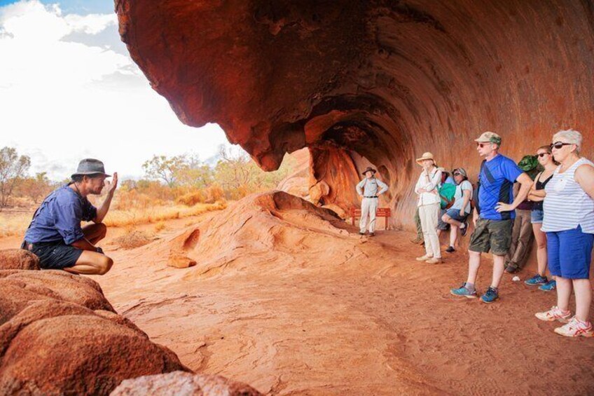 A group of people observing a large red rock formation with a cave-like opening. 5