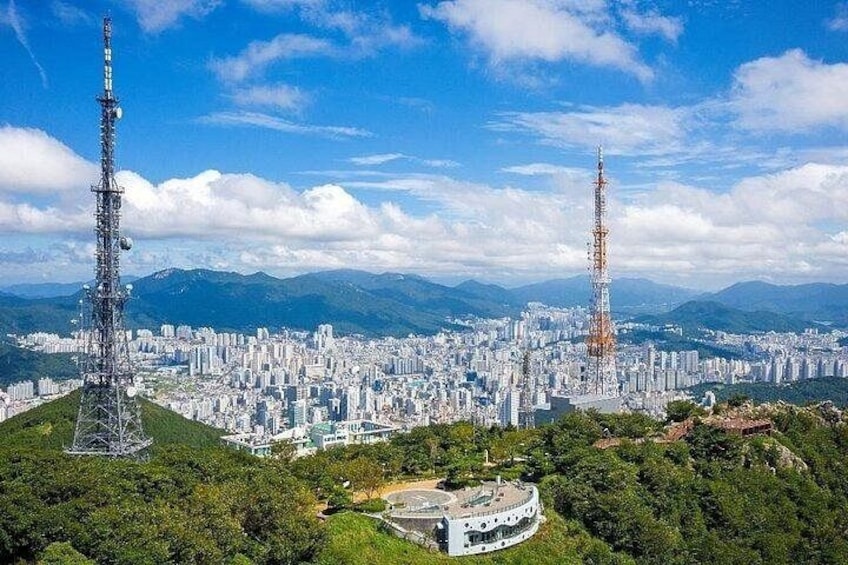 Un paisaje urbano con dos torres de comunicación destacadas, una zona densamente poblada y un fondo montañoso. 3
