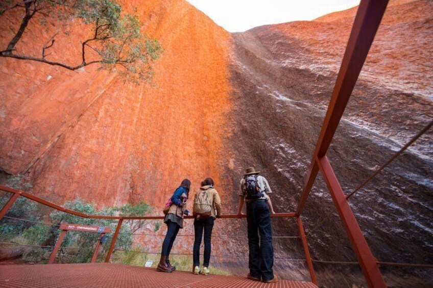 A group of people standing on a viewing platform, looking at a large red rock formation. 3