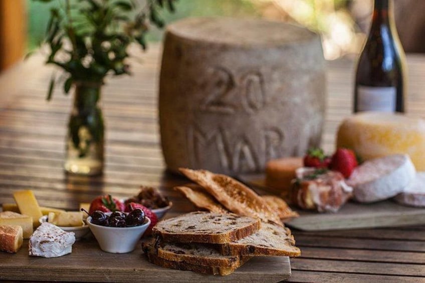 A wooden table with various cheeses, bread, and a bottle of wine. 3