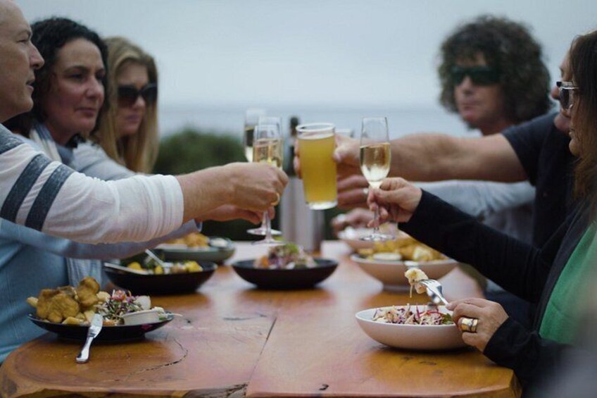 A group of people toasting with drinks around a wooden table with food. 5