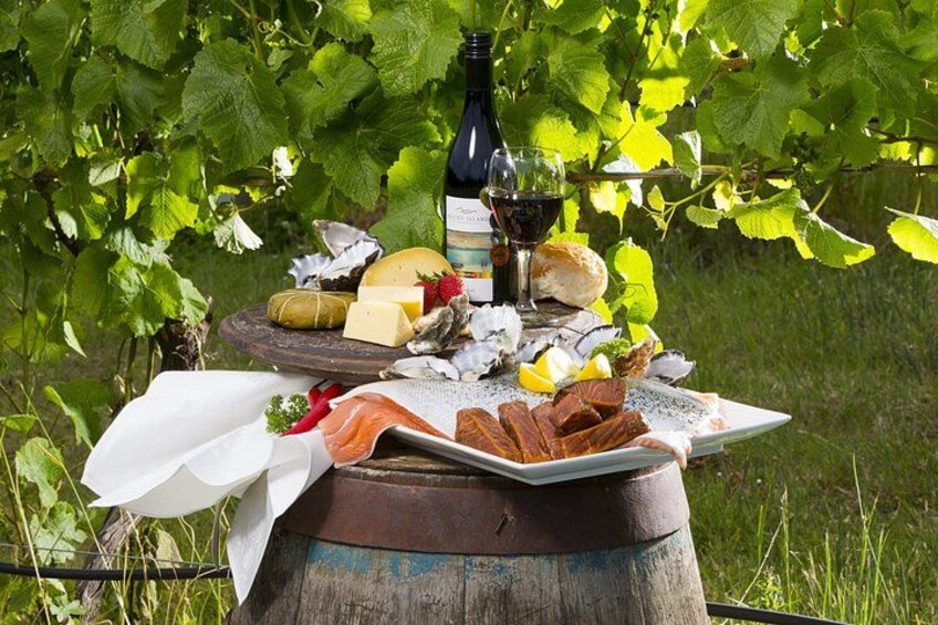 A picnic setup with cheese, bread, and wine on a wooden barrel, surrounded by greenery. 2