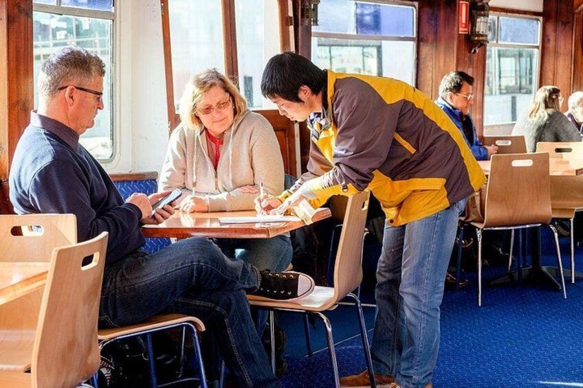 Een groep mensen zit aan tafels in een ruimte met houten wanden en grote ramen. 5
