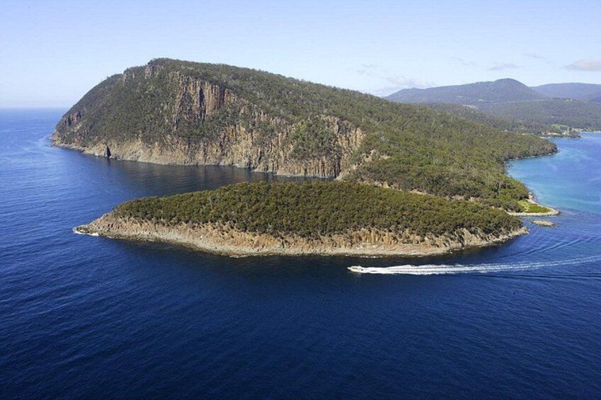 A coastal landscape with a prominent island surrounded by deep blue waters, a clear sky, and distant mountains. 2