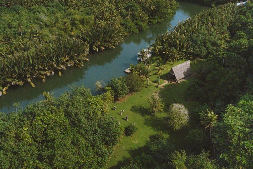 Un río rodeado de densa vegetación tropical, una casa pequeña y un cielo despejado. 1